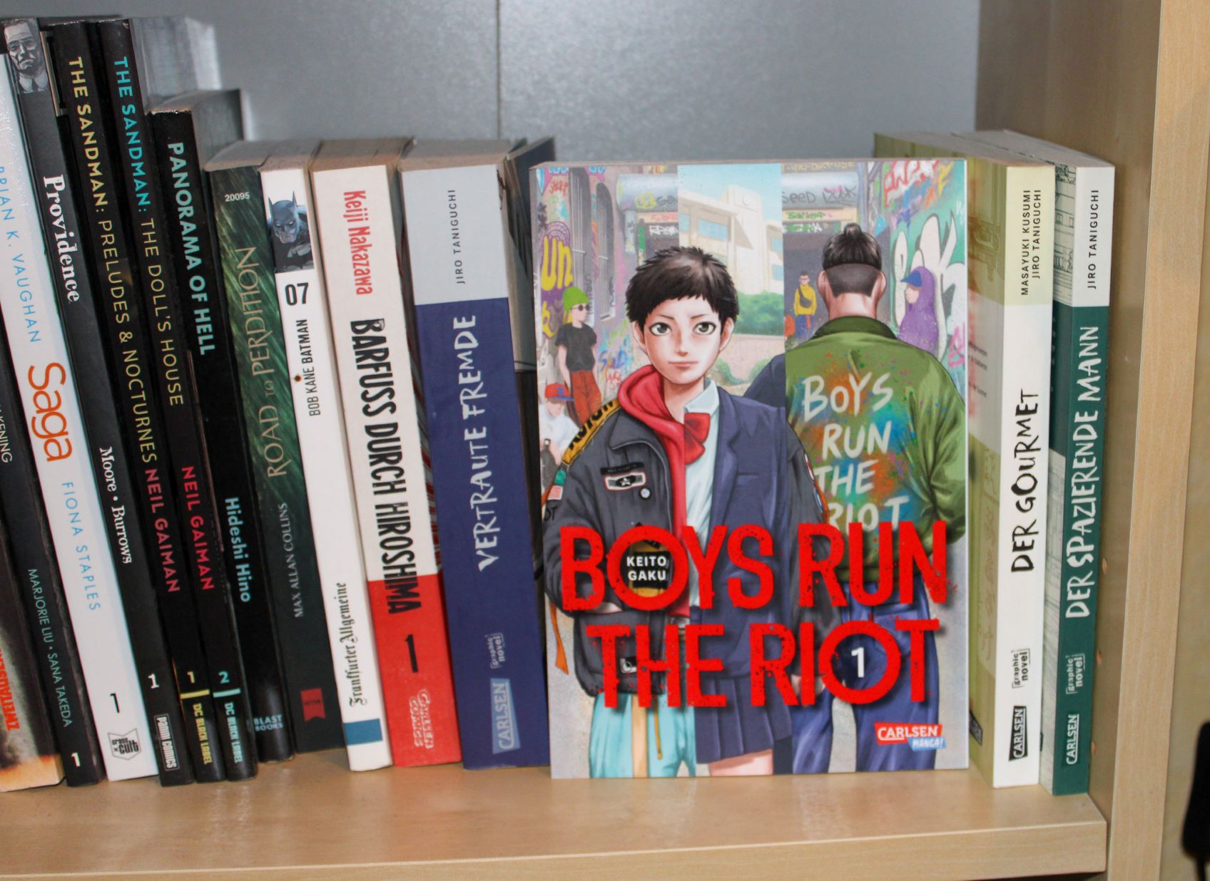 Gebundene deutsche Ausgabe von "Boys Run The Riot 1" mit Cover nach vorne in einem Bücherregal vor einer Reihe anderer Mangas fotografiert.