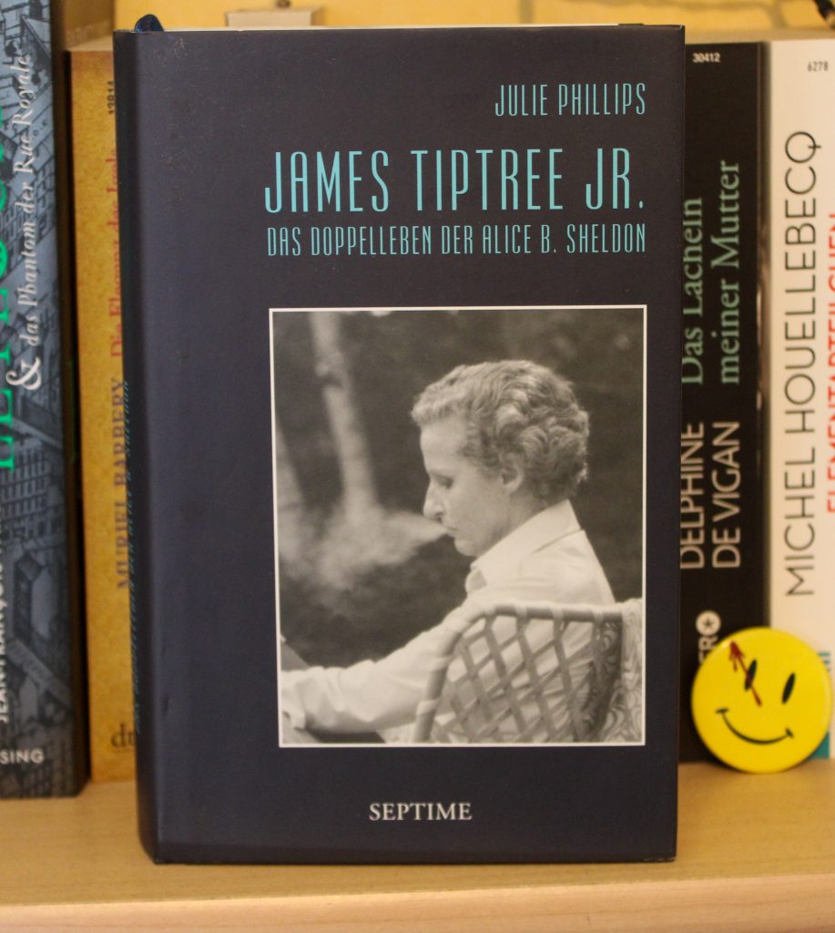 Hardcoverausgabe des Buchs "James Tiptree Jr. - Das Doppelleben der Alice B. Sheldon" von Julie Phillips, fotografiert in einem Bücherregal mit dem Cover nach vore, das ein Foto der ca. 50jährigen Alice B. Sheldon im Seitenprofil zeigt.