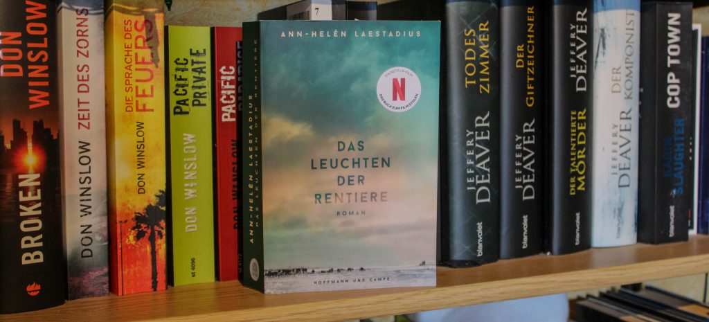 Taschenbuchausgabe von "Das Leuchten der Rentiere" mit dem Cover nach vorne in einem Bücherregal stehend.