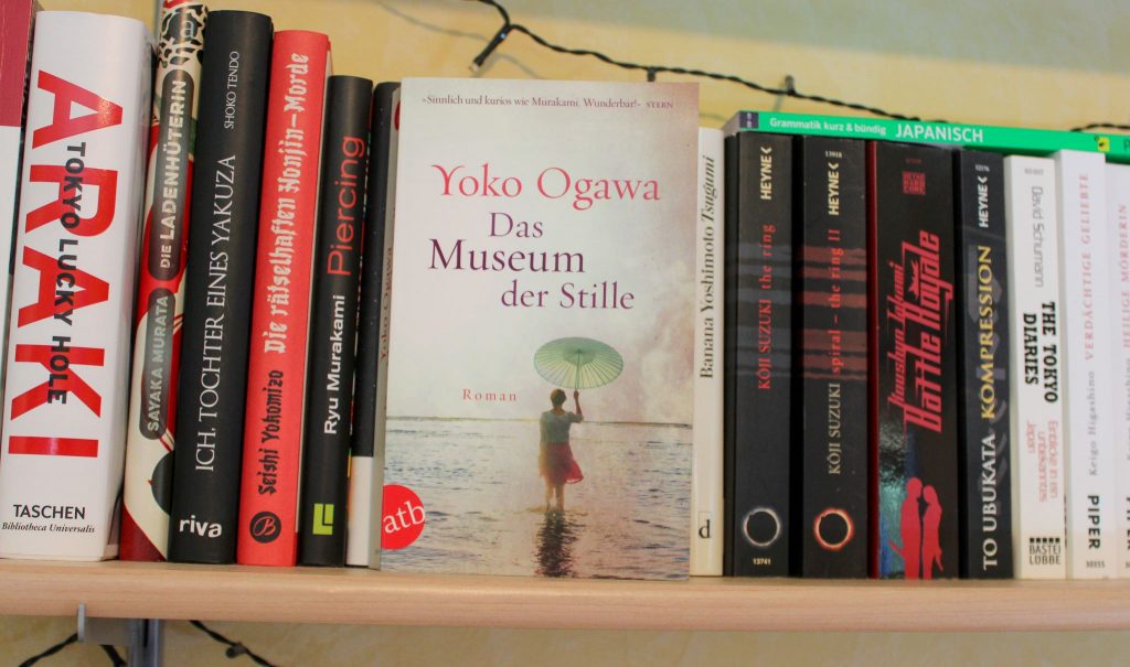 Taschenbuchausgabe von Yoko Ogawas "Das Museum der Stille", mit dem Cove nach vorne vor anderen Bücher in einem Regal stehend.
