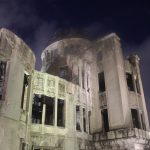 Das Friedensdenkmal in Hiroshima. Die ausgebombte Ruine eines mehrstöckigen älteren Gebäudes aus Stein mit Kuppeldach, hier bei Nacht und angeleuchtet aus der Nähe fotografiert.