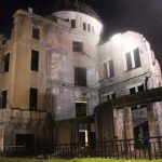 Das Friedensdenkmal in Hiroshima. Die ausgebombte Ruine eines mehrstöckigen älteren Gebäudes aus Stein mit Kuppeldach, hier bei Nacht und angeleuchtet aus der Nähe fotografiert.