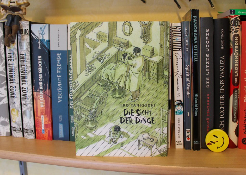Taschenbuchausgabe des Mangas "Die Sicht der Dinge". Auf dem Cover sehen wir einen Friseursalon. Im hinteren Teil schneidet ein Mann einem anderen Mann die Haare, im Vordergrund spielt ein kleiner Junge auf dem Boden.